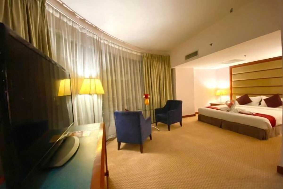 Ein Hotelzimmer mit einem Bett, einem Schreibtisch mit Lampe, einem Sessel und einem Fernseher.