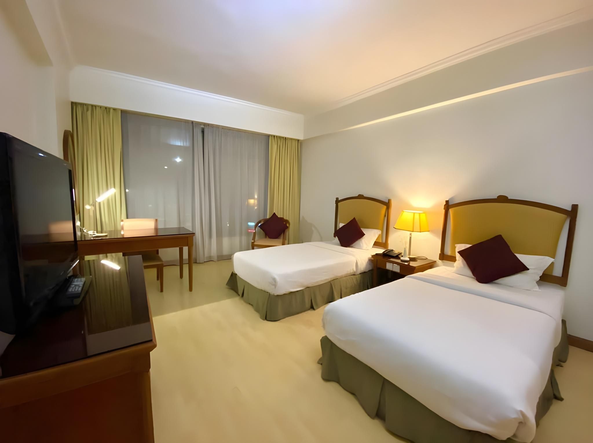 Habitación de hotel con dos camas, un escritorio, un televisor y una ventana con cortinas.