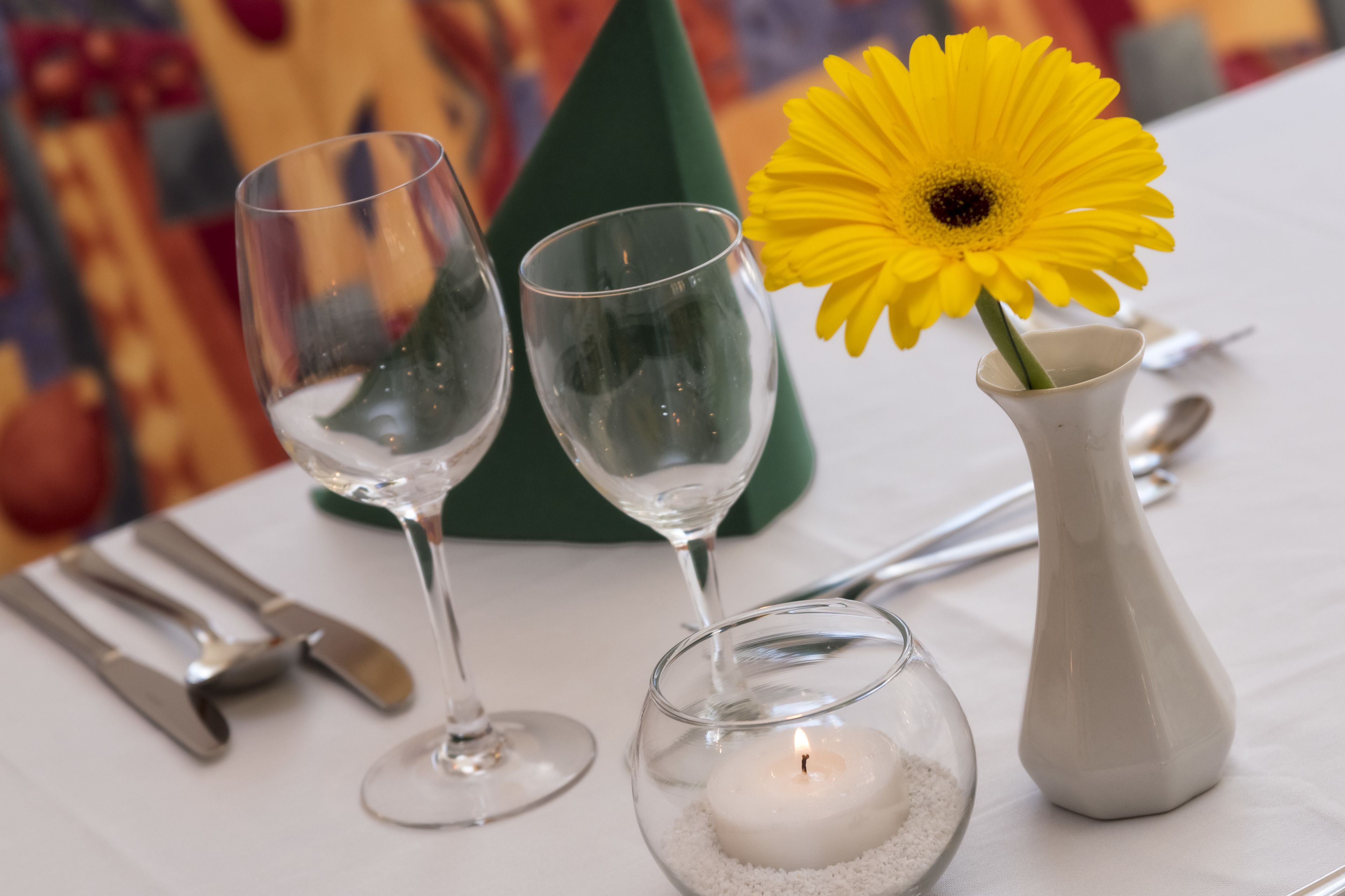 Een gedekte tafel met twee wijnglazen, een kaars en een vaas met een gele bloem.