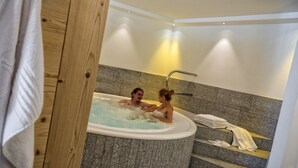 A couple in a jacuzzi with a stone wall and a towel rack. - Hotel Elisabeth (Chienes)