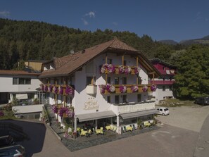 Et hotel med en balkon dekoreret med blomster, udendørs siddepladser og udsigt over den omkringliggende skov.