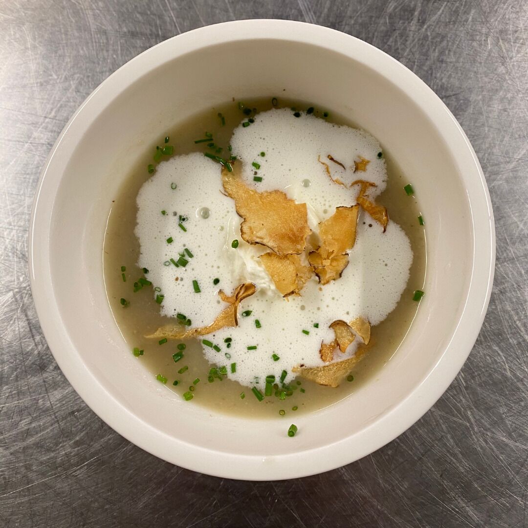 Eine Schale Suppe mit cremiger Konsistenz, verziert mit grünen Kräutern und knusprigen Elementen.