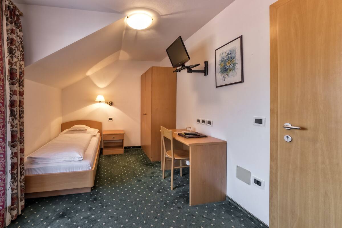 Una habitación de hotel pequeña con una cama individual, un escritorio y una silla.