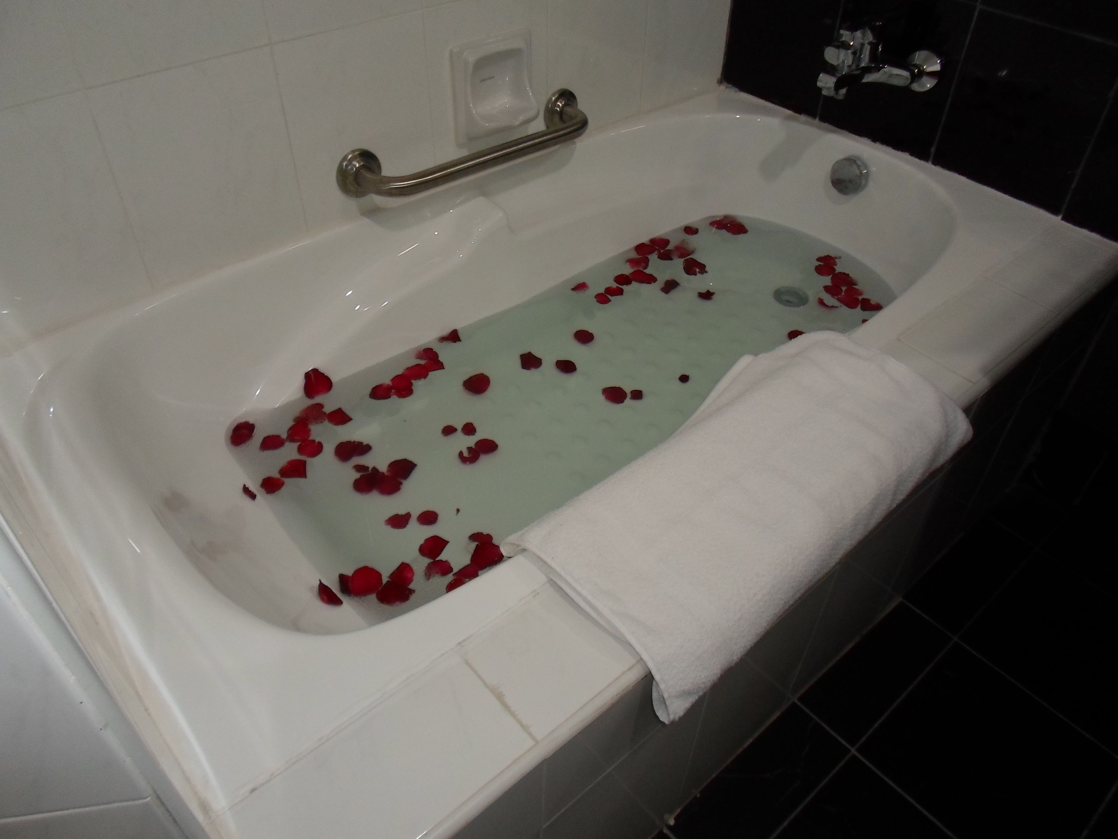 Uma banheira com pétalas de rosas e uma toalha branca.