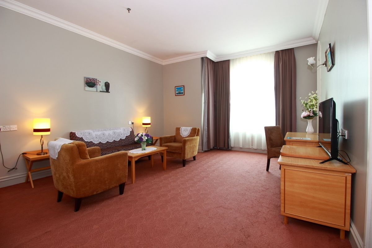 A hotel room with a sofa, armchairs, a small table, a TV, and a desk.
