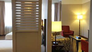 Habitación de hotel con dos camas, un escritorio, una silla, una lámpara y una ventana con cortinas.