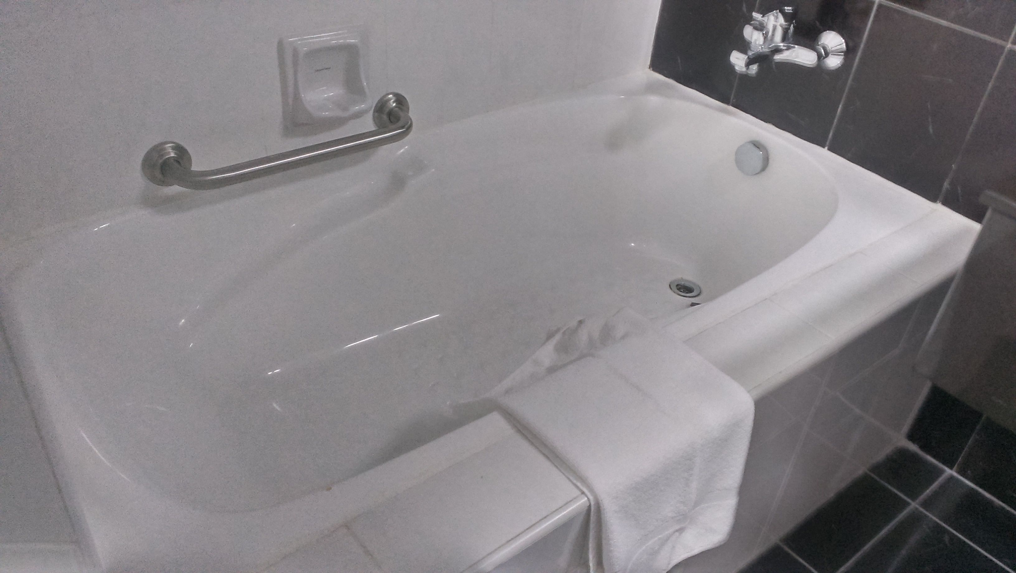 Una bañera blanca con un asidero, una toalla y un desagüe.