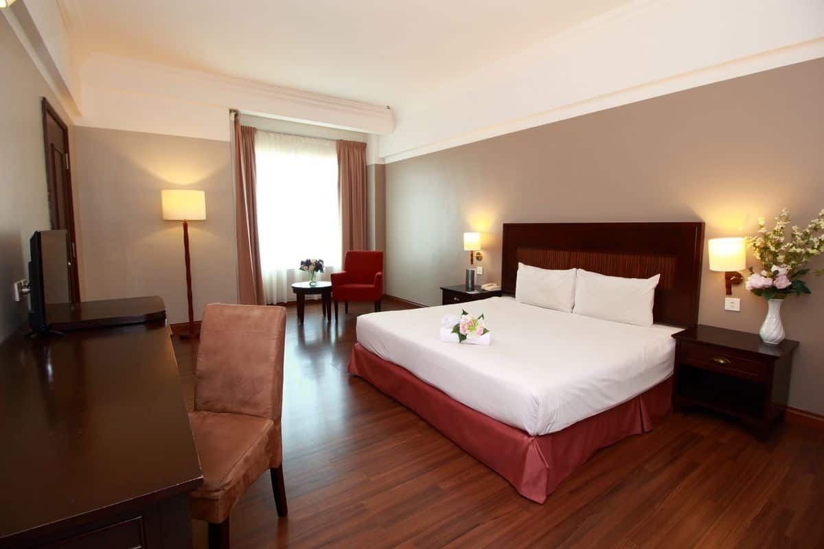 A hotel room with a large bed, a desk, a chair, a small table, and two bedside lamps.