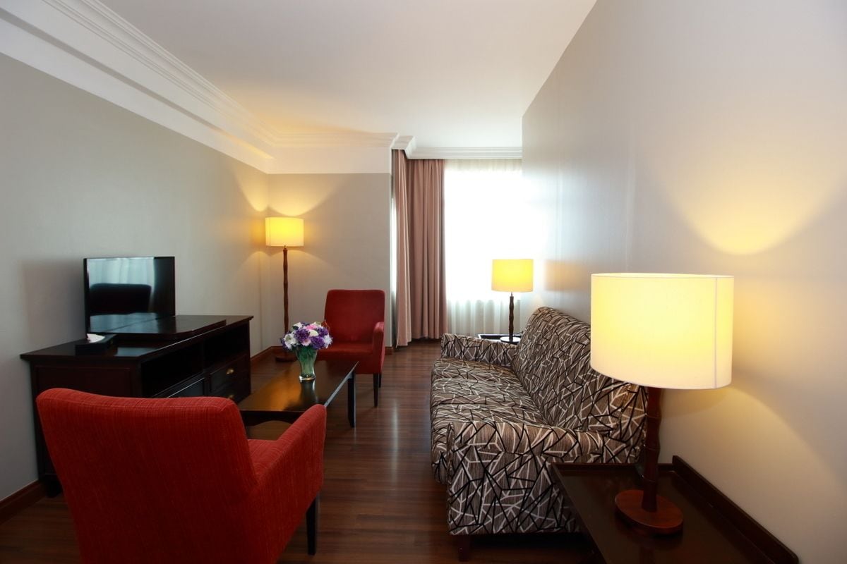Una habitación de hotel con sofá, un sillón rojo, televisión, escritorio y dos lámparas.