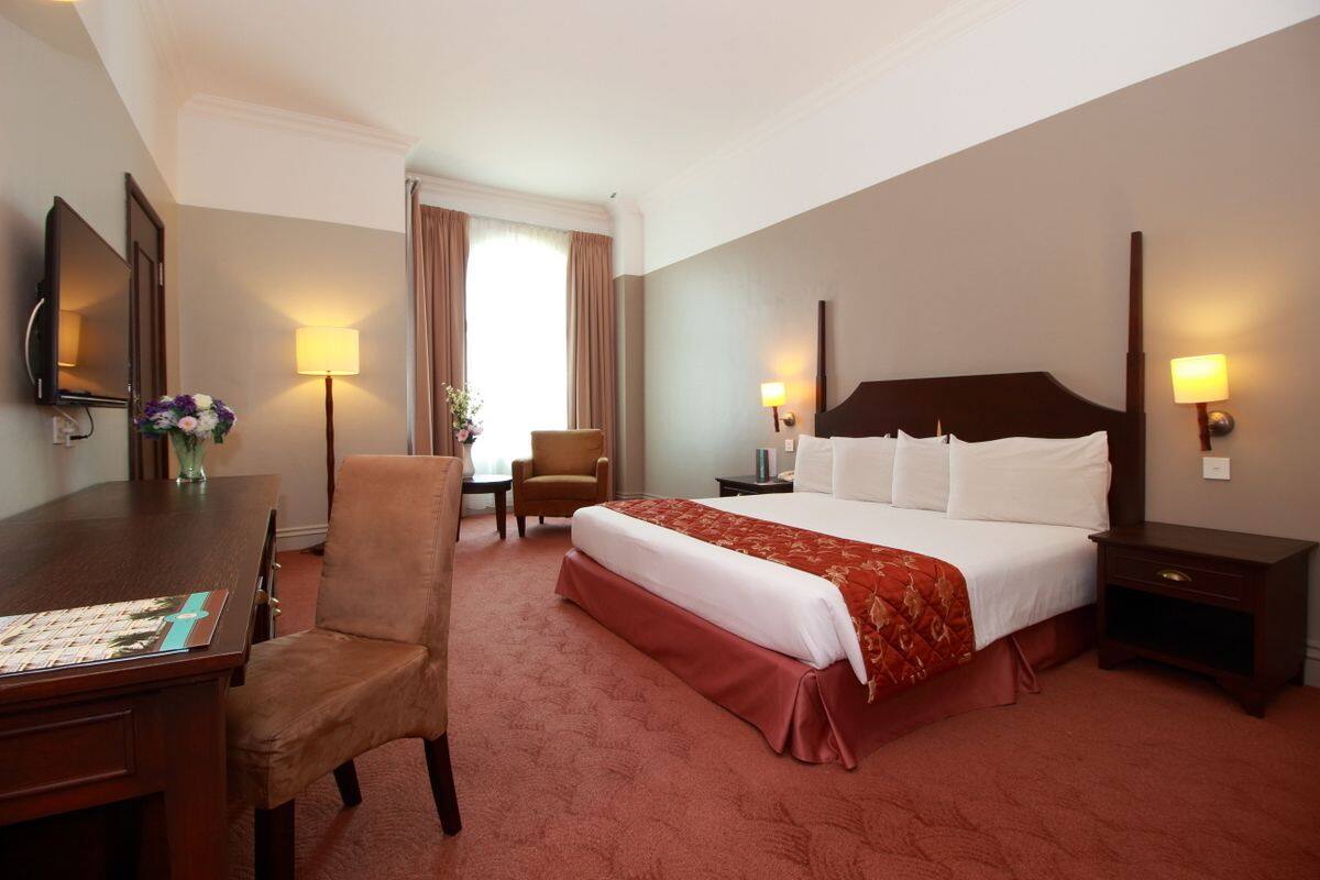 A hotel room with a large bed, a desk, a chair, and two bedside lamps.