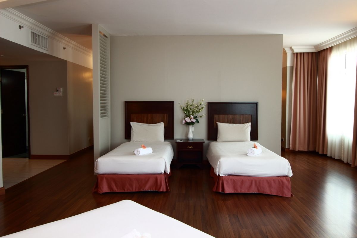 Une chambre d’hôtel avec deux lits, une table de chevet ornée d’un vase de fleurs et une grande fenêtre avec des rideaux.