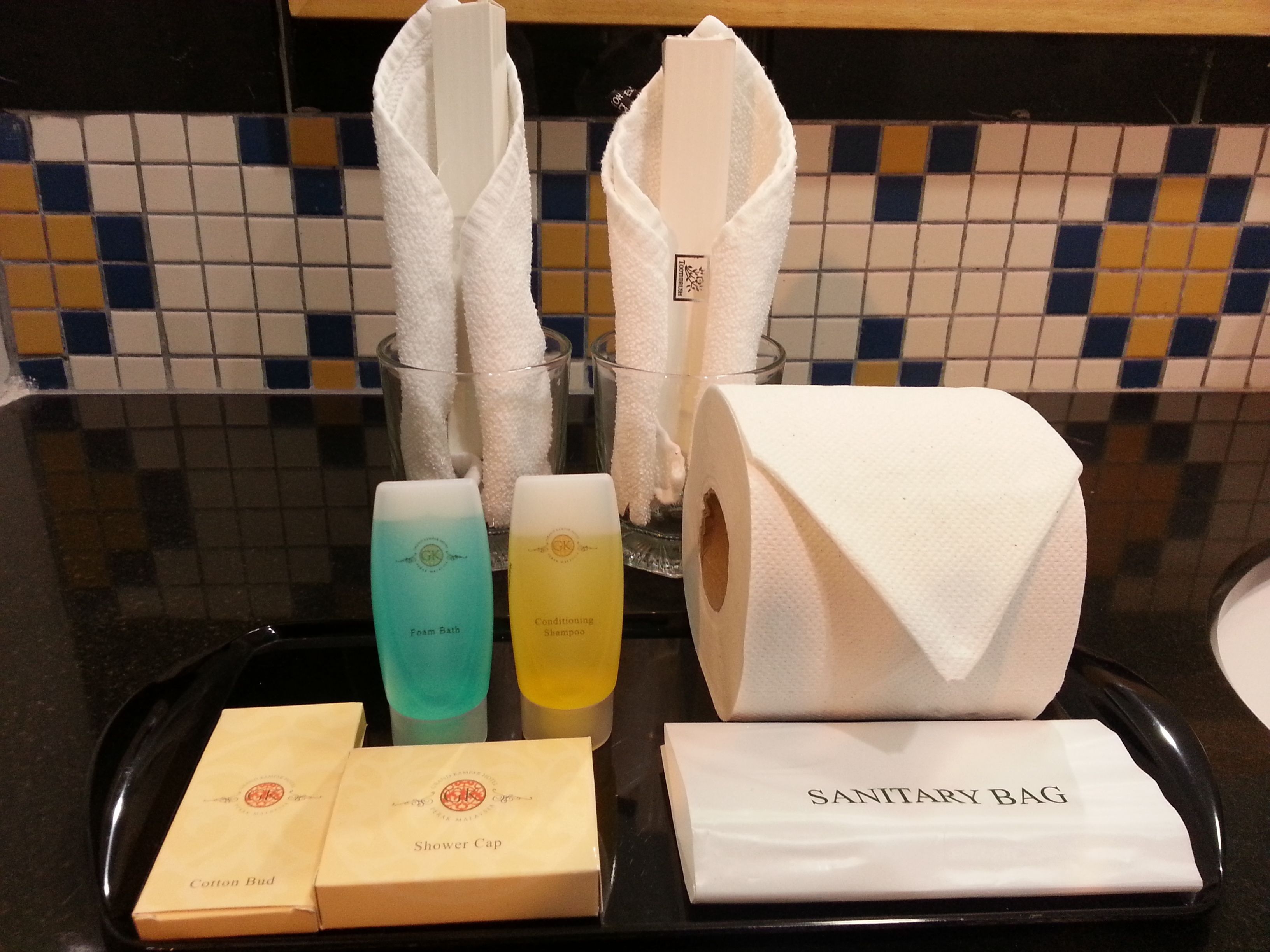 A tray with toiletries including a shower cap, cotton bud, sanitary bag, and two bottles of shampoo.