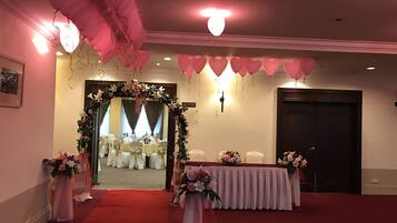 Una habitación con alfombra roja, sillas blancas, un arco floral y globos rosados.