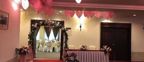 A room with a red carpet, white chairs, a floral archway, and pink balloons.