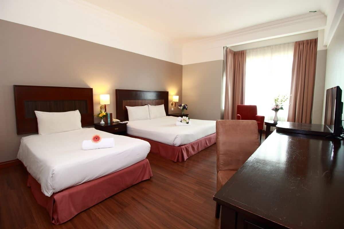 A hotel room with two beds, a wooden desk, a chair, a TV, and a window with curtains.