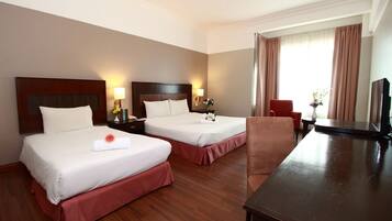 A hotel room with two beds, a wooden desk, a chair, a TV, and a window with curtains.