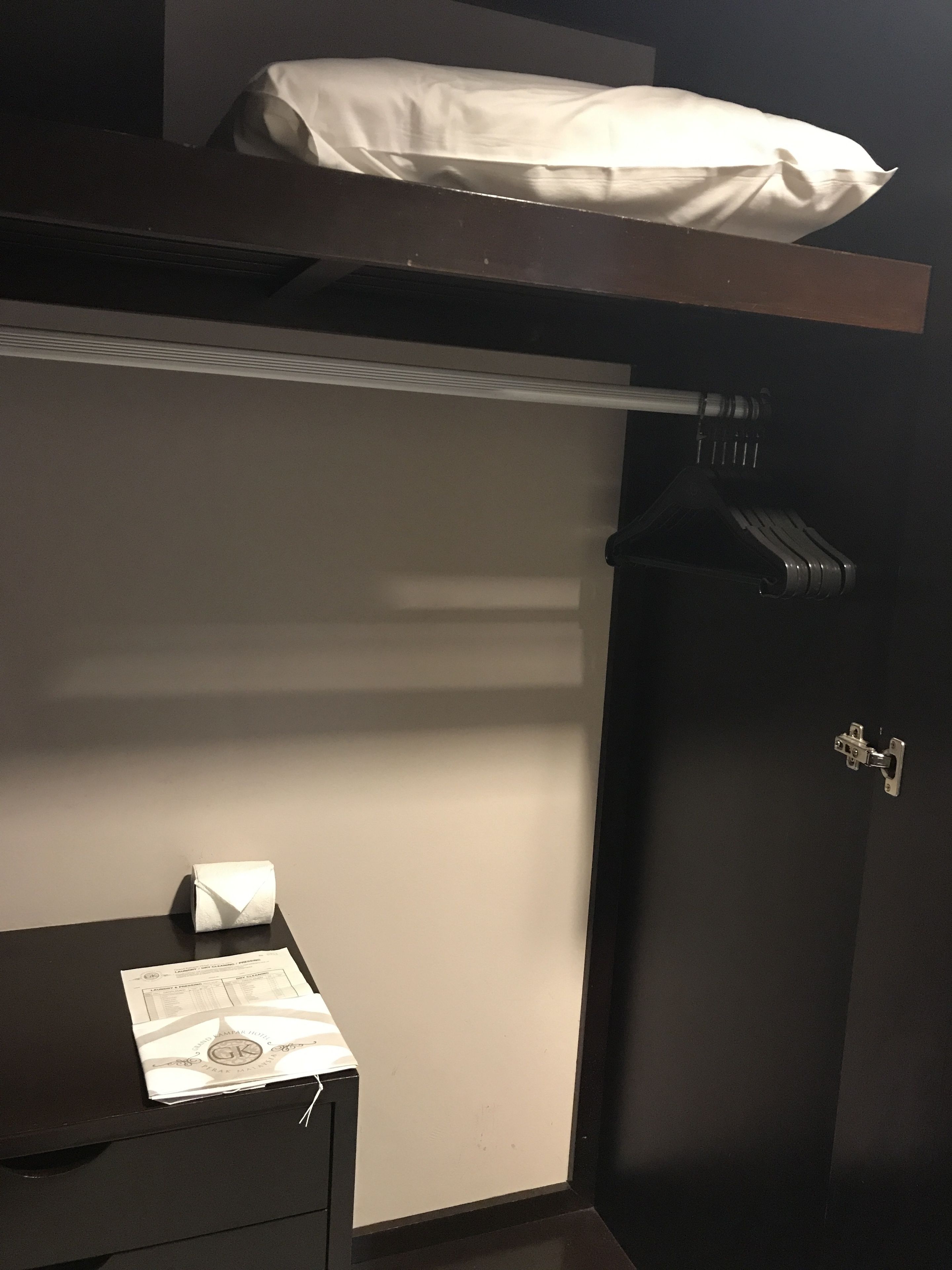 Una habitación pequeña con una cama individual superpuesta, un armario y un escritorio con una caja de pañuelos y un menú.
