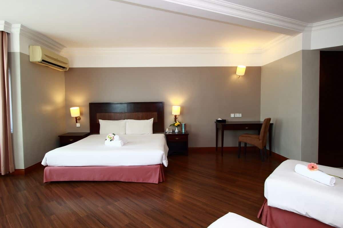 A hotel room with a double bed, a desk, a chair, and an air conditioning unit.