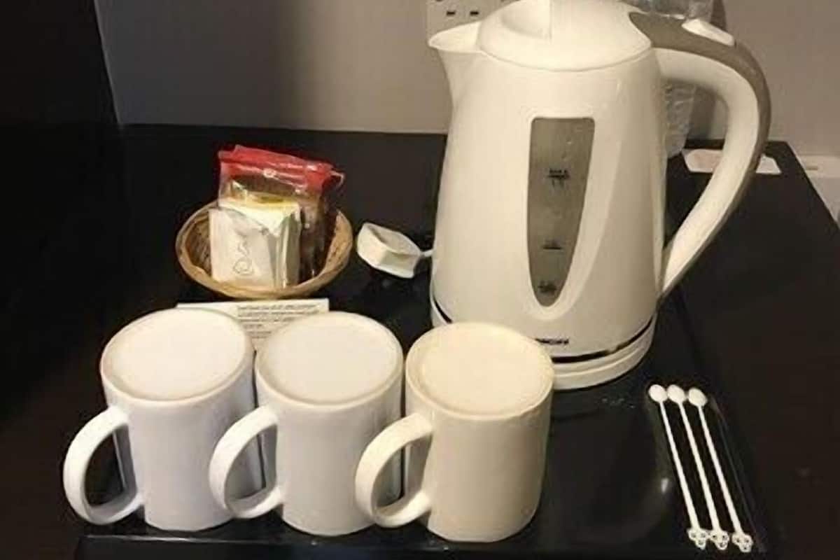 A kitchen setup with a kettle, three mugs, a small bowl with a packet, and two bottles.