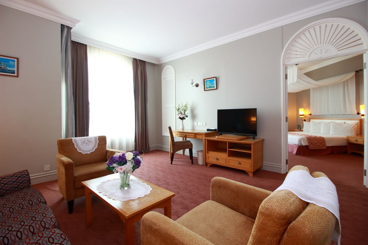A hotel room with a sofa, a TV, a desk, and a bed with a canopy.