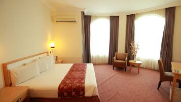 A hotel room with a large bed, a desk, a chair, and a small table.
