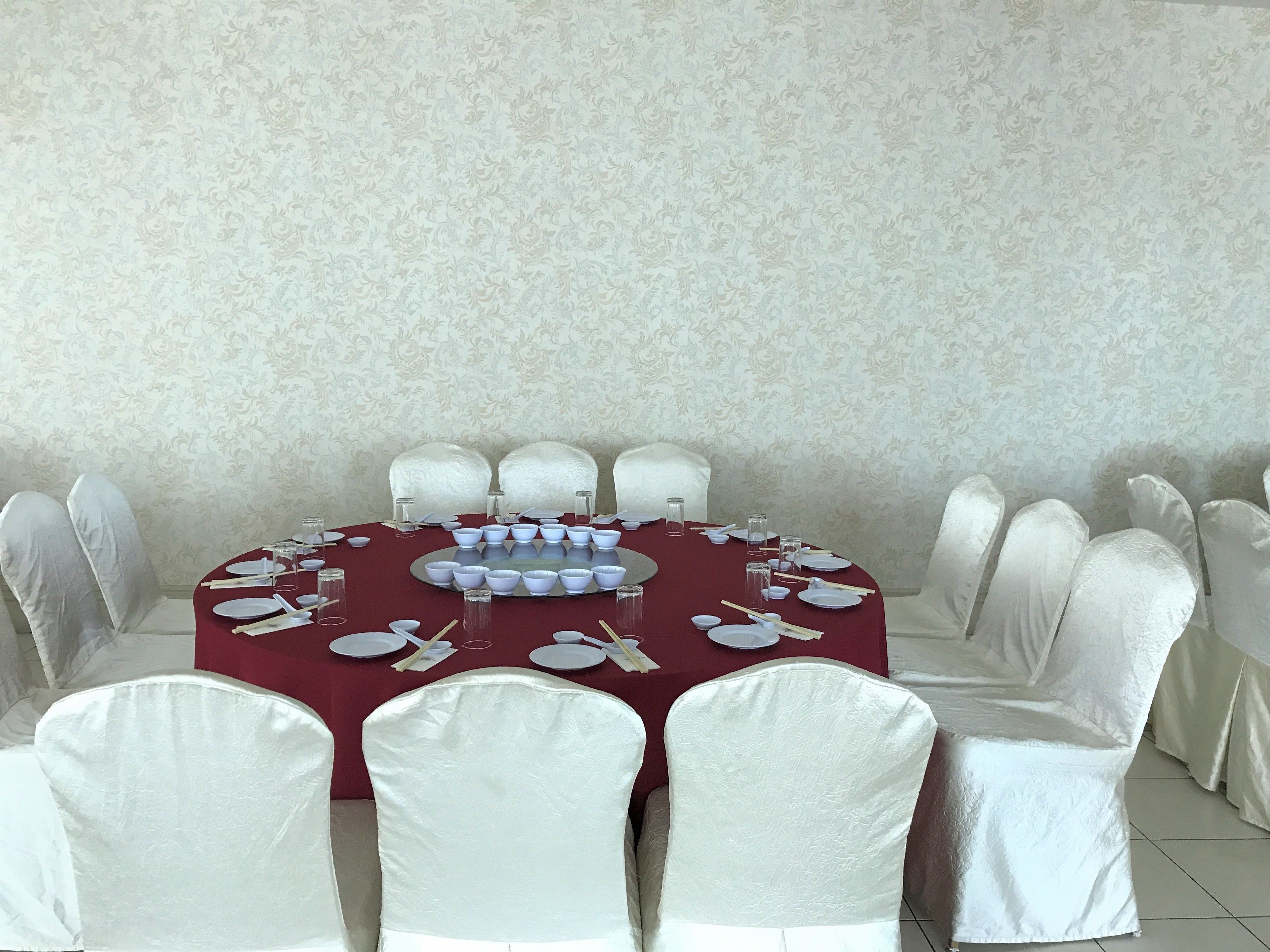 A round table with a red tablecloth, surrounded by white chairs with white seat covers.