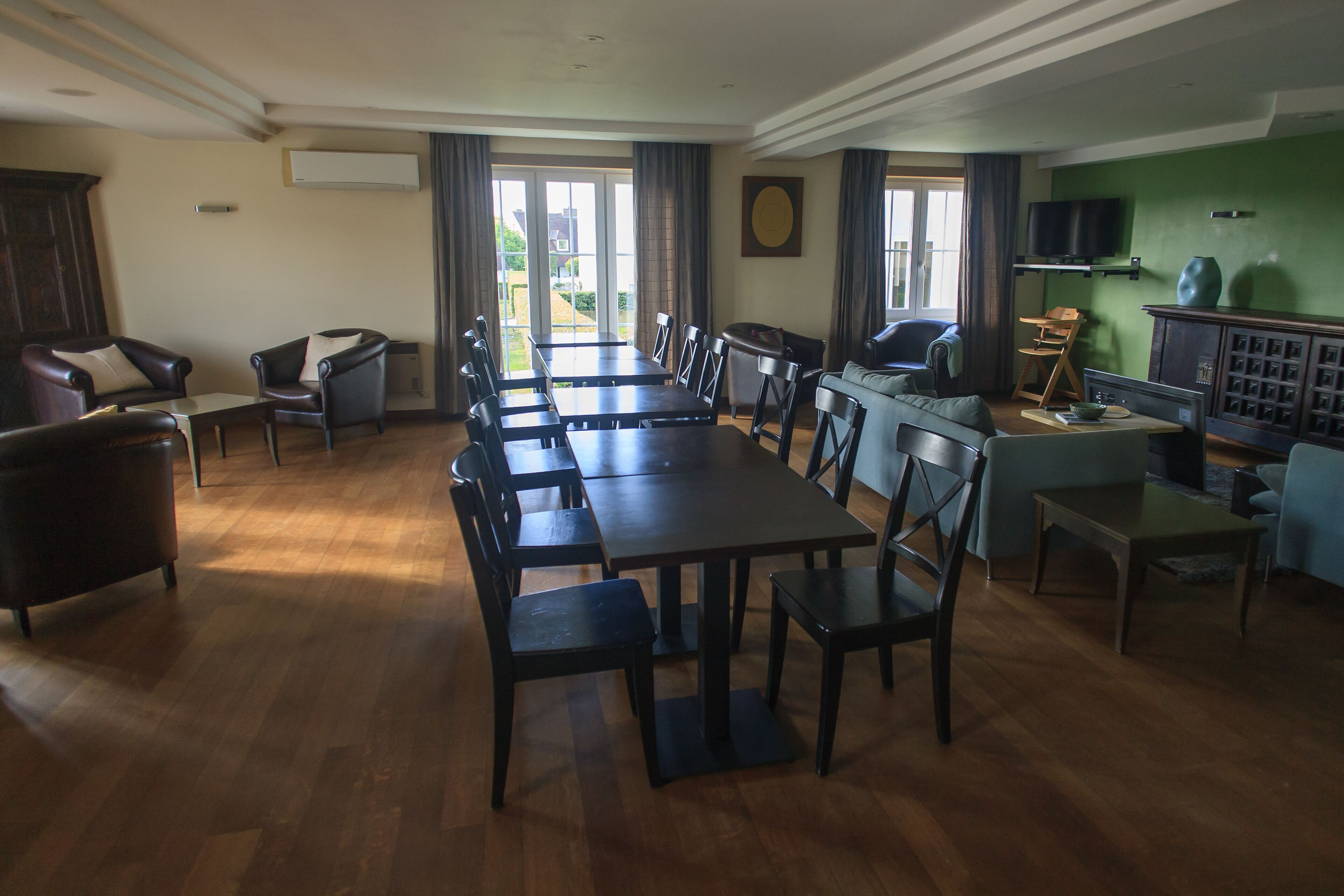 Un vaste espace de salle à manger avec une longue table et des chaises, un canapé et un téléviseur fixés sur un mur vert.