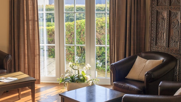 A room with a large window, a leather armchair, a wooden table, and a decorative panel. - Hotel St-Janshof (Waregem)