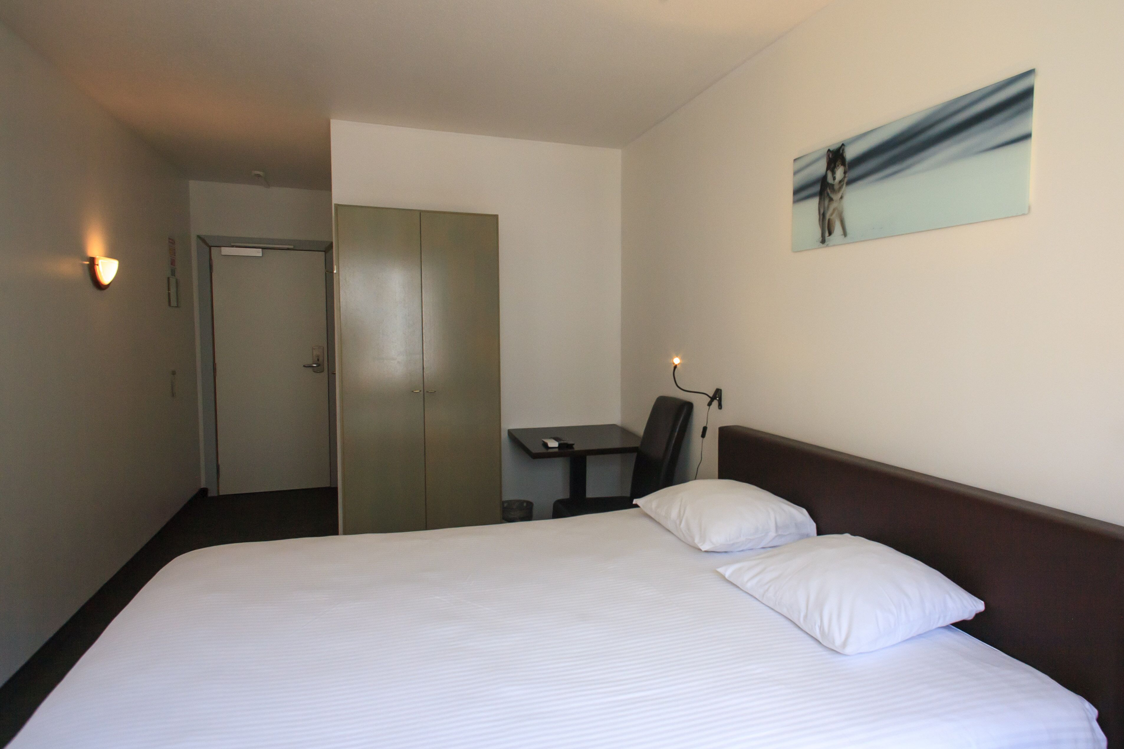 Una habitación de hotel con una cama, un escritorio, una silla y un cuadro en la pared.