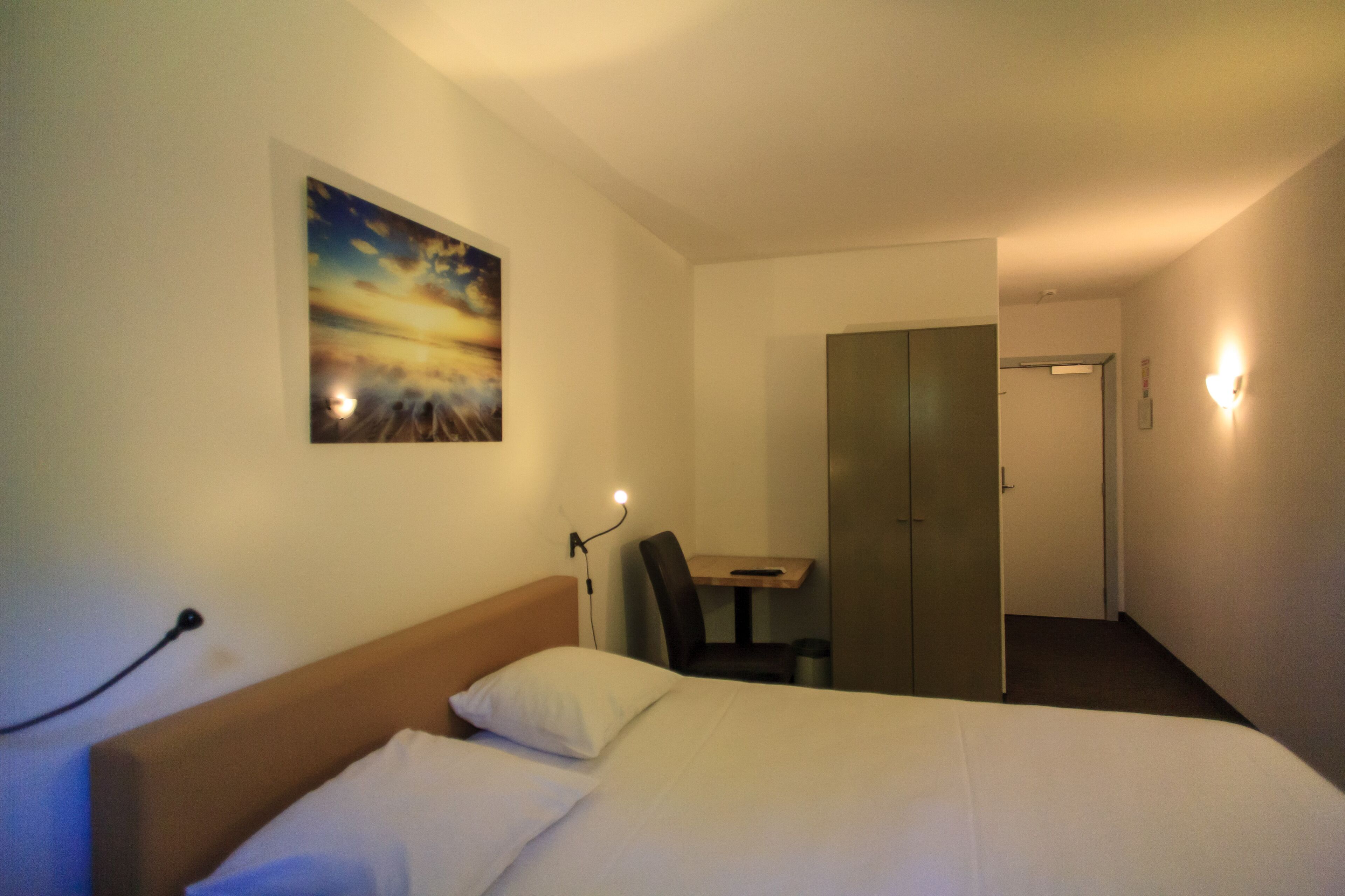 A hotel room with a bed, a desk, and a wardrobe.