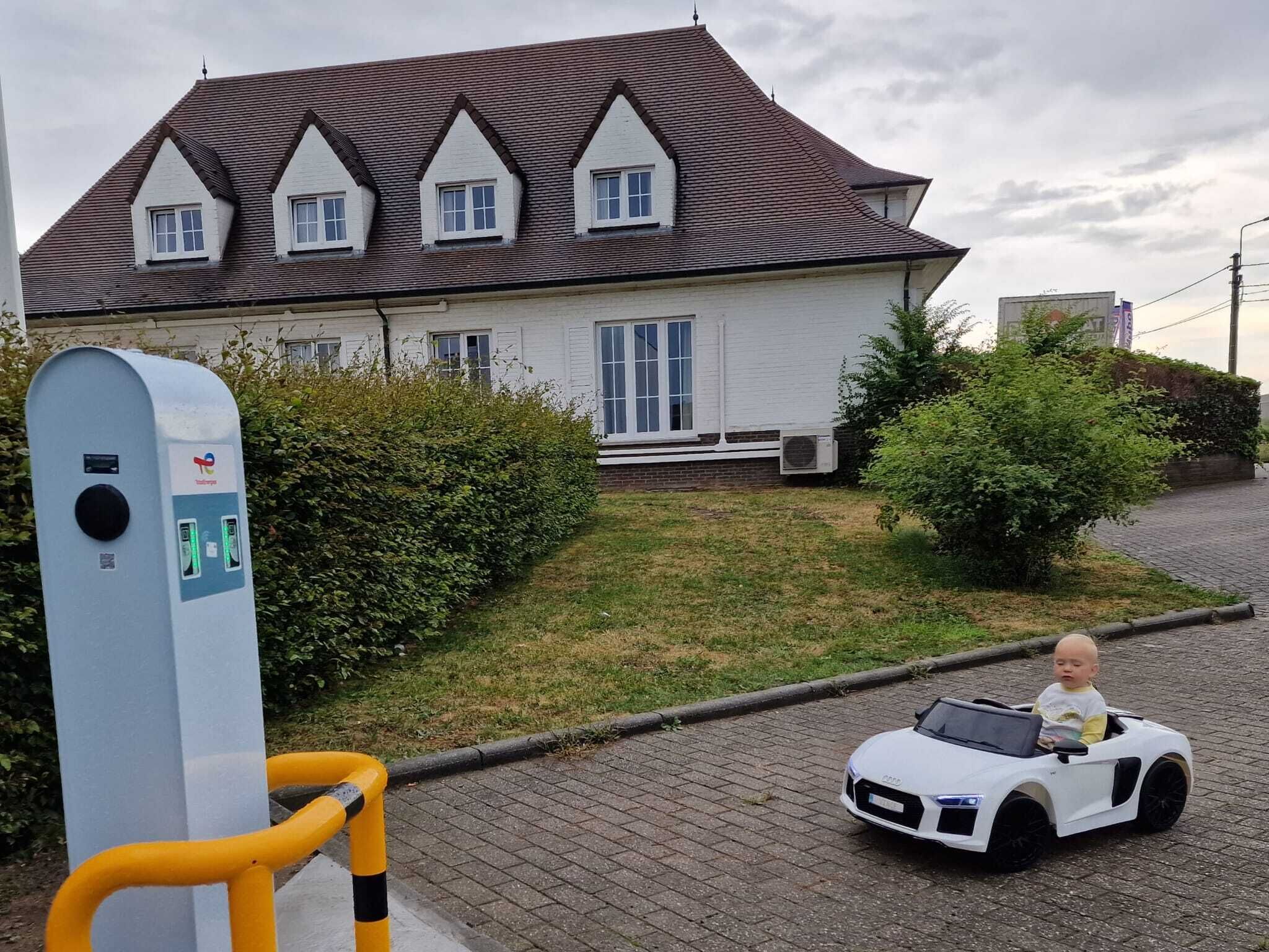 A house with a white exterior and a brown roof, a paved driveway, and a child in a toy car.