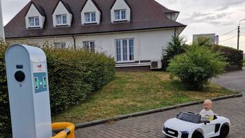 A house with a white exterior and a brown roof, a paved driveway, and a child in a toy car.