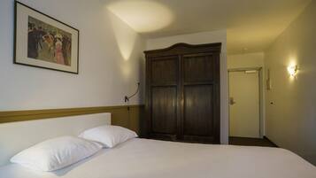 A hotel room with a bed, a large wardrobe, a framed picture on the wall, and a light fixture on the wall.