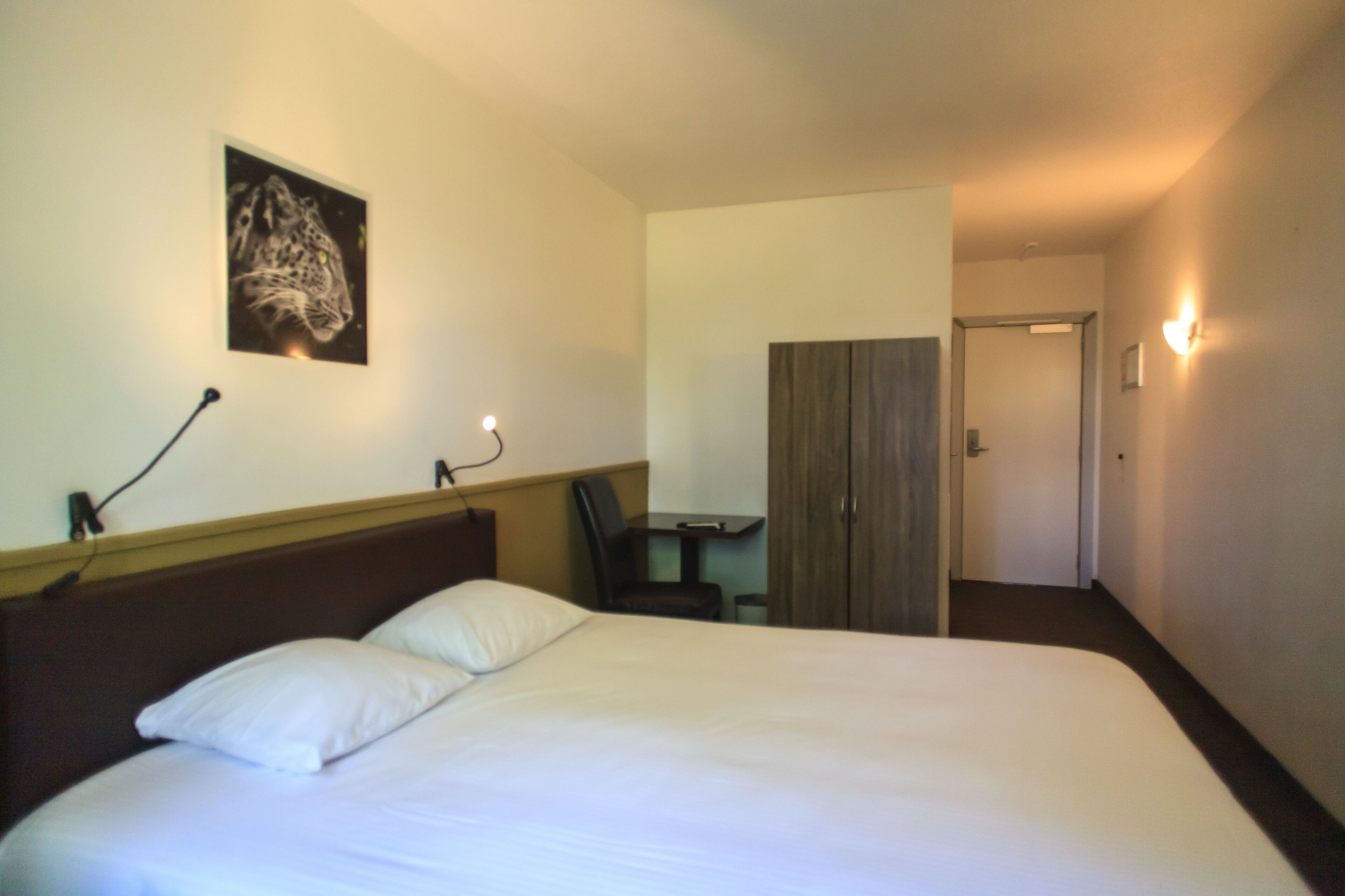 Ett hotellrum med en säng, ett skrivbord, en stol och en garderob.