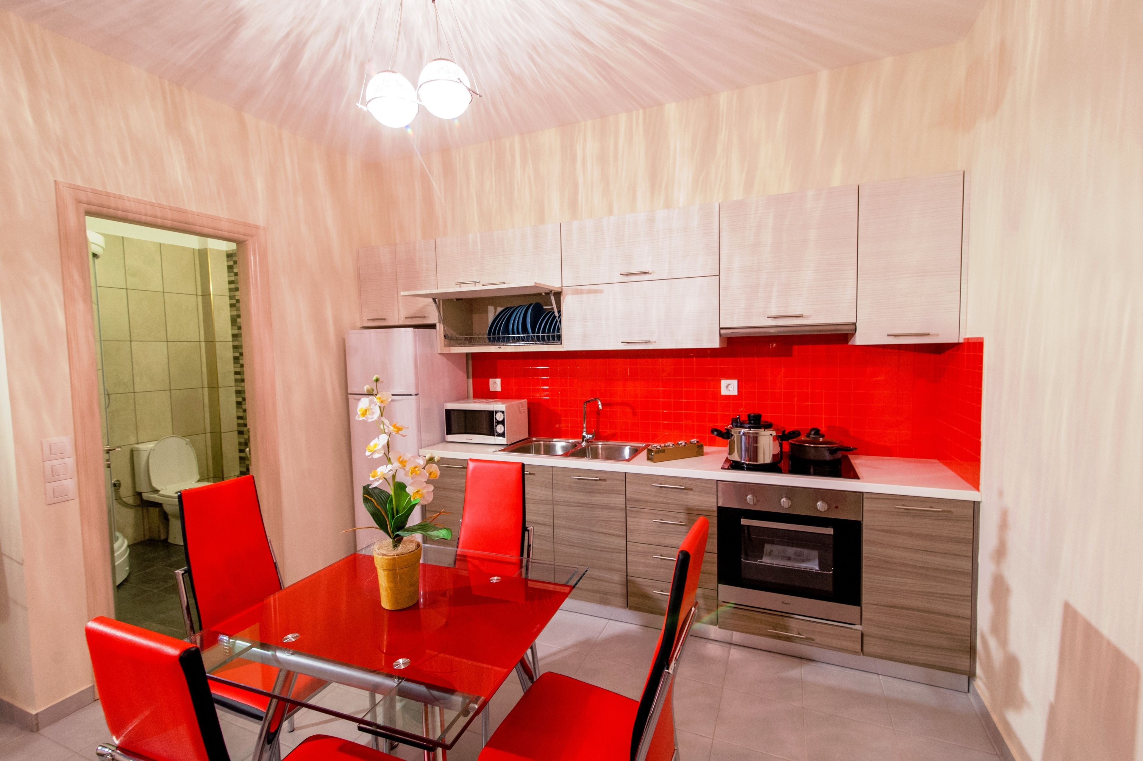 A modern kitchen with red chairs, a glass table, and stainless steel appliances.
