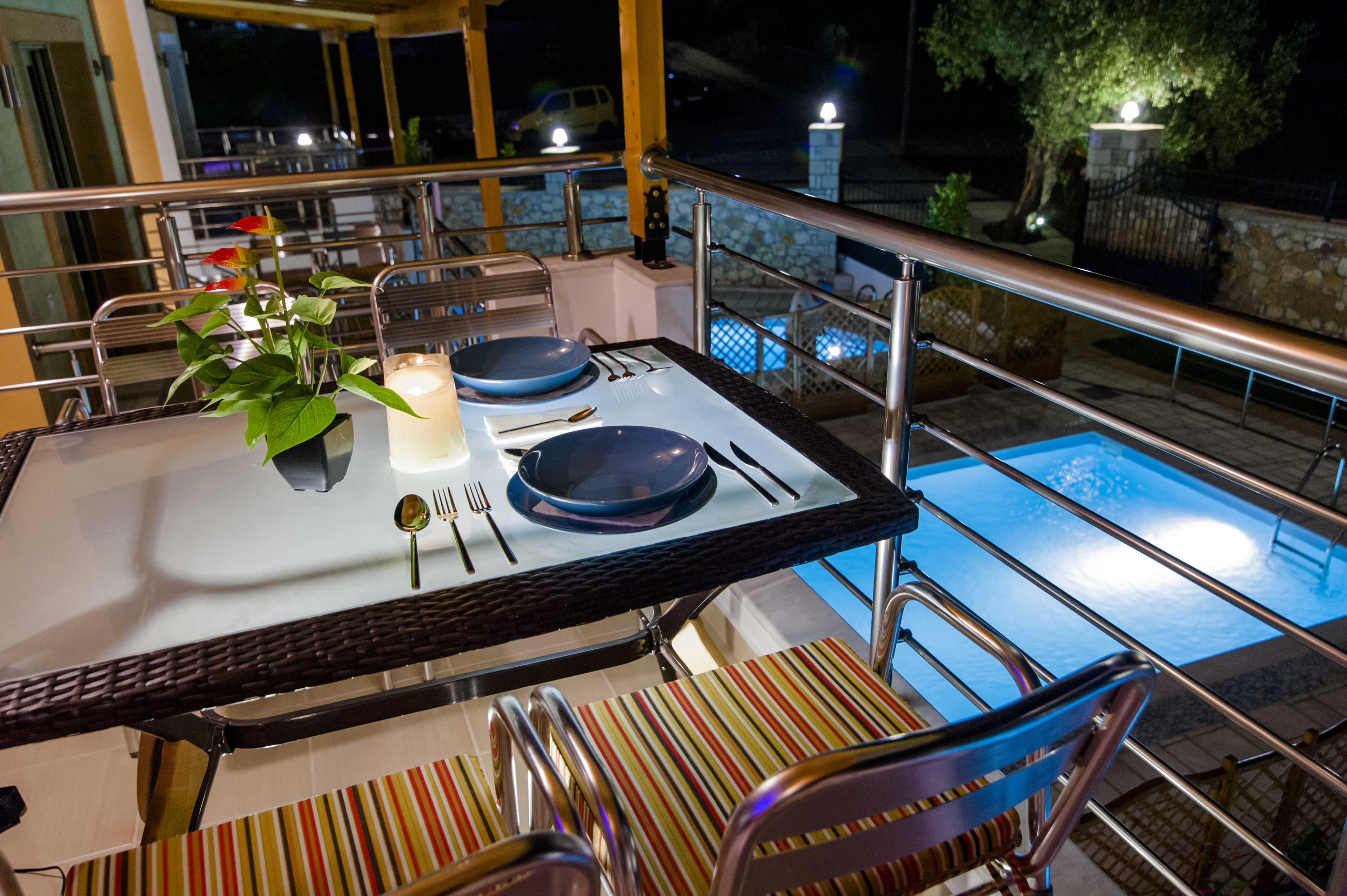 A dining table set with plates, cutlery, and a candle, overlooking a swimming pool.