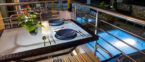 A dining table set with plates, cutlery, and a candle, overlooking a swimming pool.