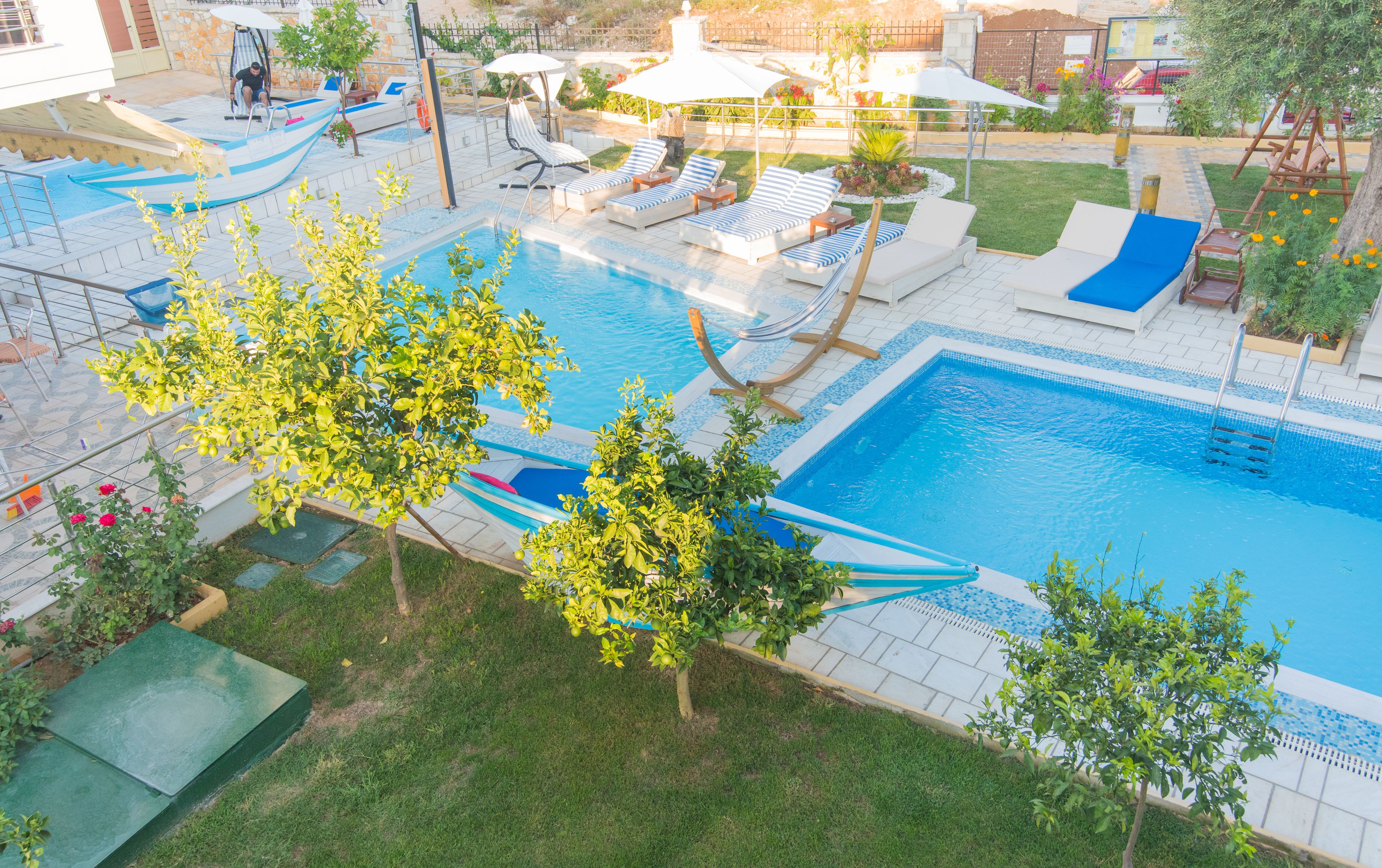 A swimming pool with multiple lounge chairs and a slide, surrounded by greenery and a tiled deck.