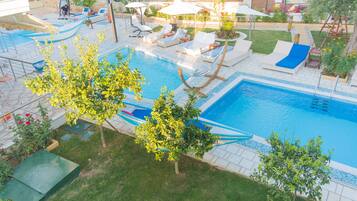 A swimming pool with multiple lounge chairs and a slide, surrounded by greenery and a tiled deck.