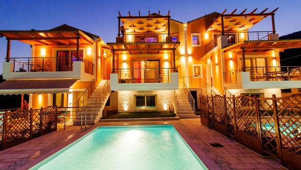 Un hotel de varios pisos con piscina, mobiliario exterior y una fachada bien iluminada.