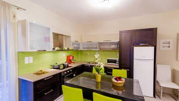 A modern kitchen with green tiles, a central island, bright green chairs, and a white refrigerator.
