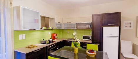 Une cuisine moderne avec des carreaux verts, un îlot central, des chaises d’un vert vif et un réfrigérateur blanc.