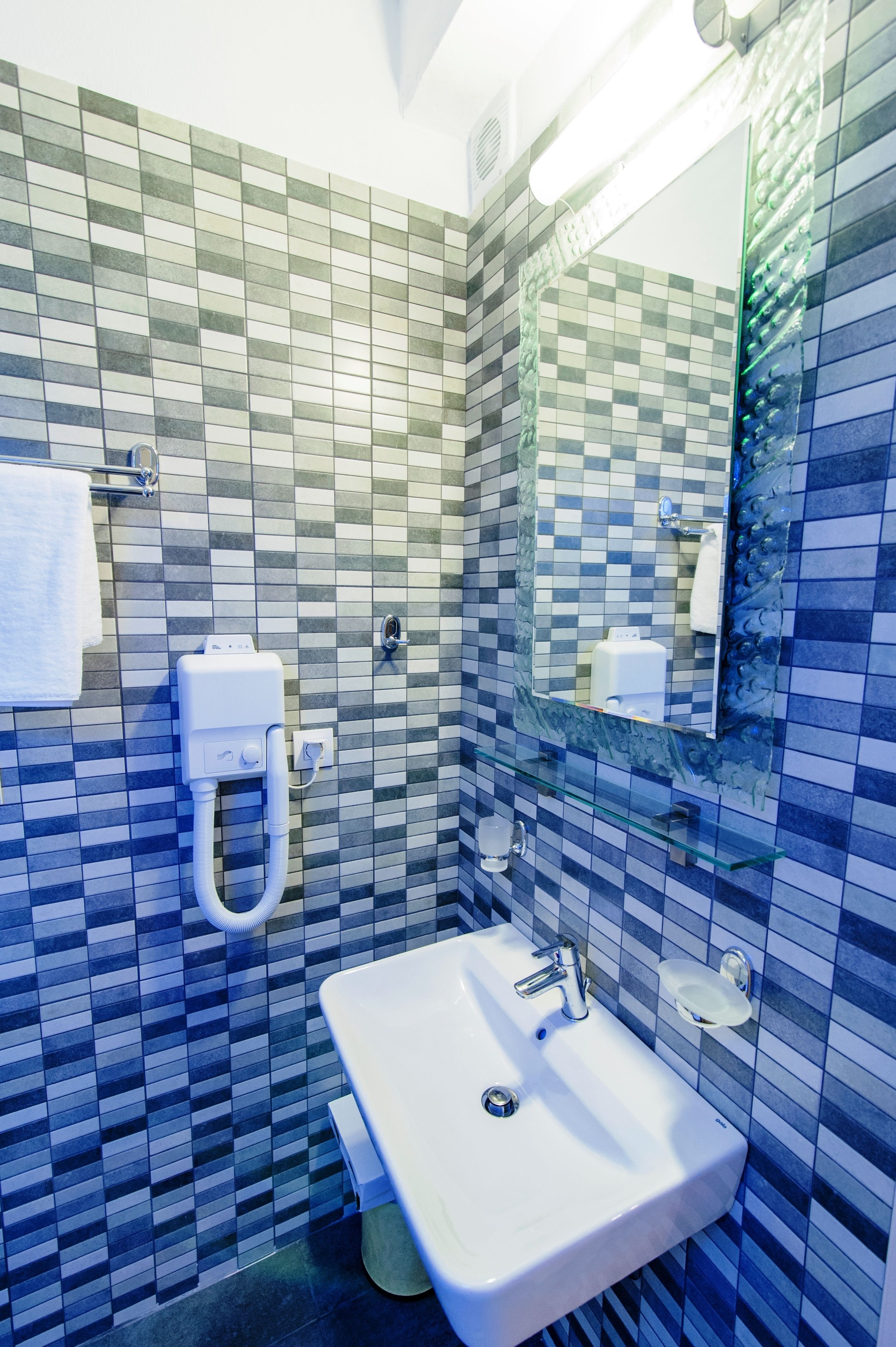 Un baño con salpicadero de azulejos, un lavamanos, un espejo y un perchero para toallas.