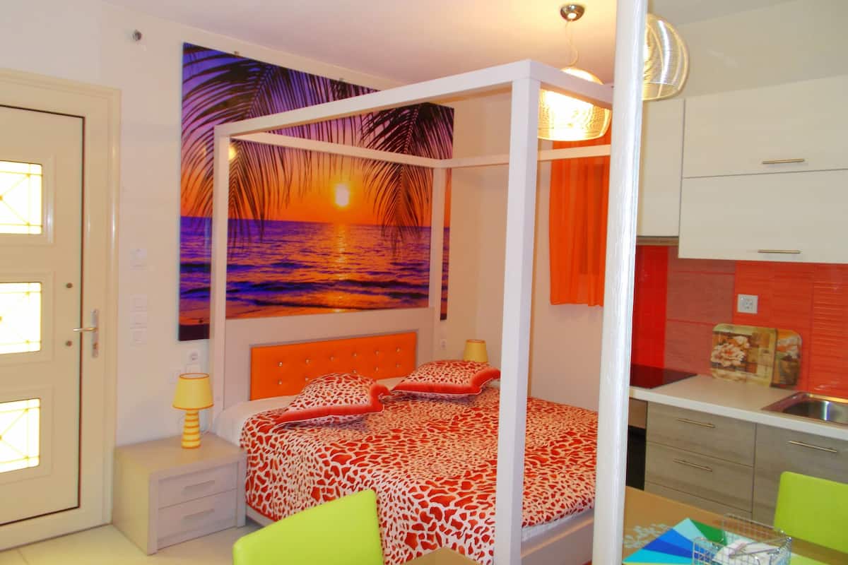 Un dormitorio con cama con dosel, una mesita de noche, una lámpara, un cuadro de un atardecer y vistas a la cocina.