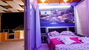 Un dormitorio con cama, ventana con vistas a un pueblo y balcón con barandilla.