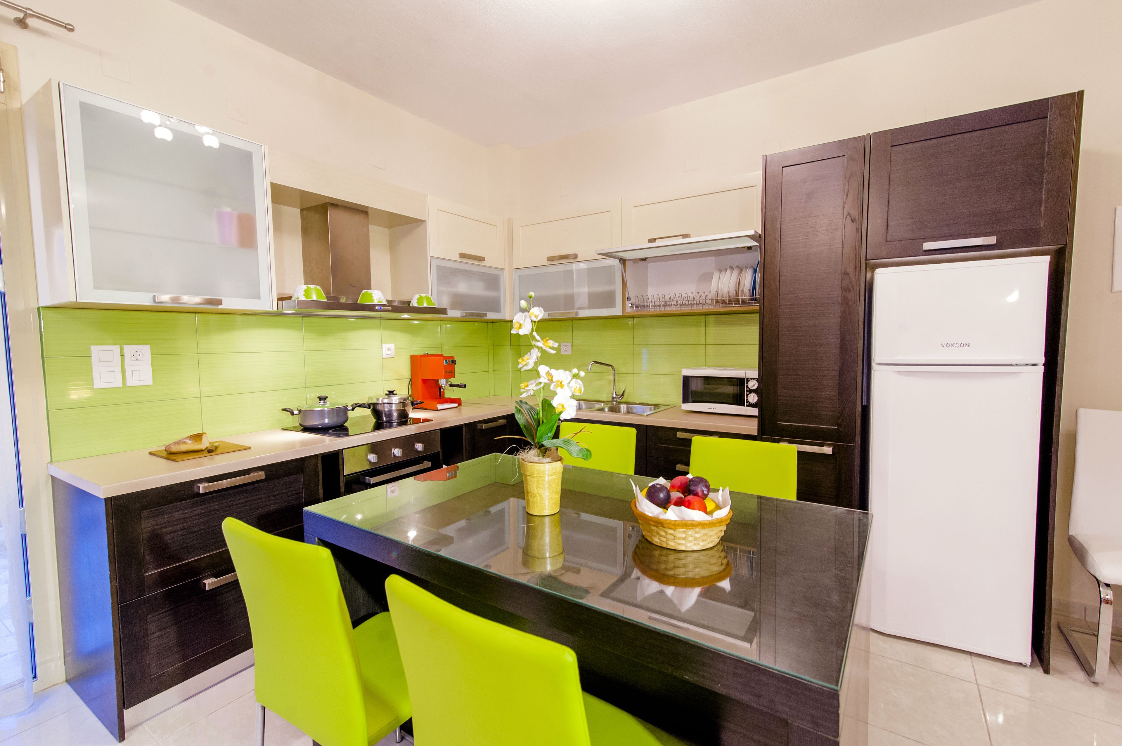 Een moderne keuken met een centraal eiland, felgroene stoelen en een koelkast.