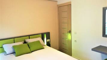 Una habitación de hotel con una cama, cabecera verde, puerta de madera y un estante pequeño.