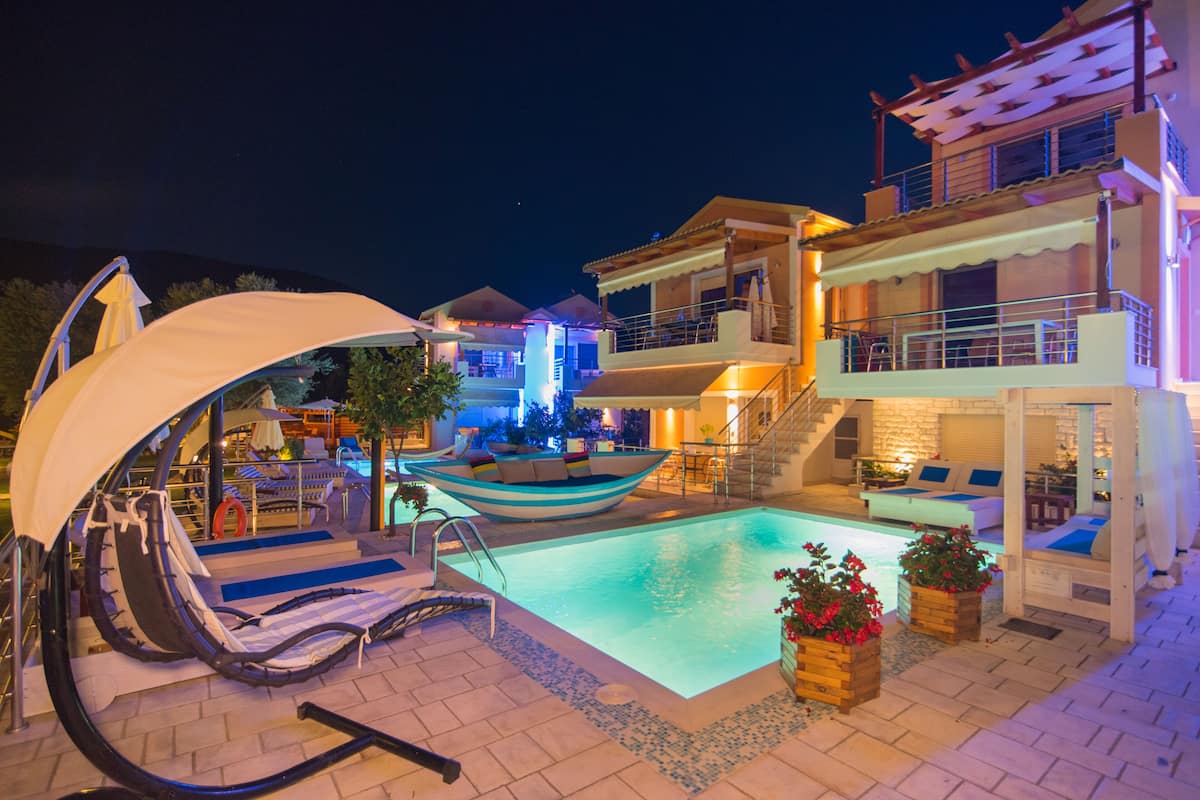 Zona de piscina con sillones de descanso, una fuente con forma de barco y un edificio de varios niveles con balcones.