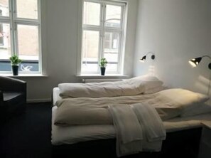 A bed with white bedding, two potted plants by the window, and two wall-mounted lamps.