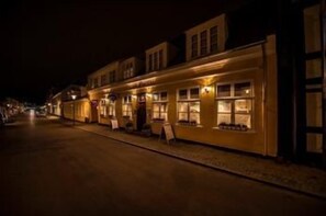 A row of buildings with illuminated windows, a paved street, and a signboard.